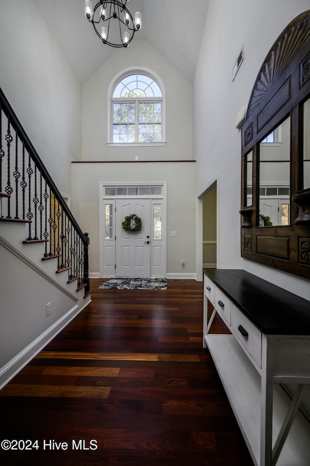 entrance foyer with dark wood-type flooring, high vaulted ceiling, a healthy amount of sunlight, and a notable chandelier