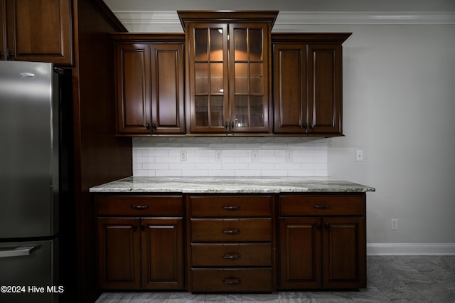 kitchen with light stone countertops, dark brown cabinetry, stainless steel refrigerator, and backsplash