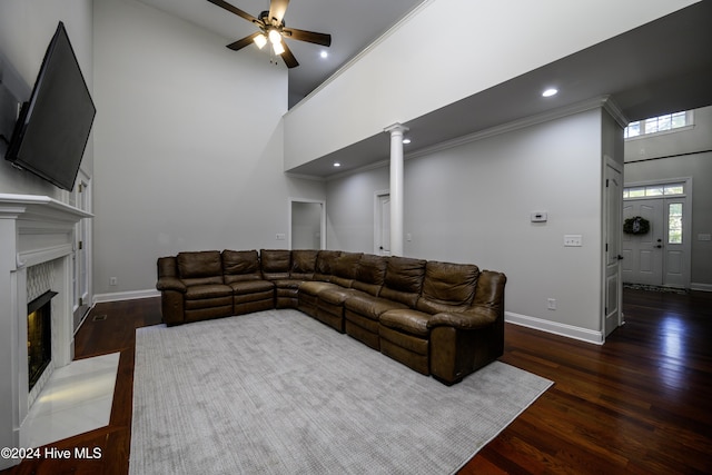 living room with ceiling fan, dark hardwood / wood-style flooring, decorative columns, crown molding, and a towering ceiling