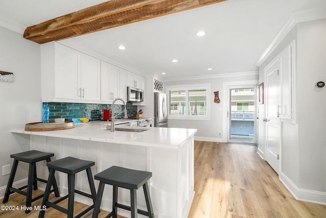 kitchen featuring kitchen peninsula, a breakfast bar, stainless steel appliances, light hardwood / wood-style floors, and white cabinetry