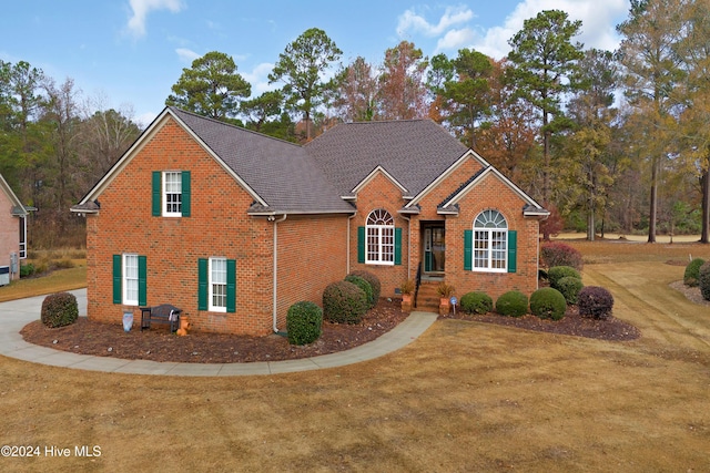 traditional-style home with roof with shingles, brick siding, and a front lawn