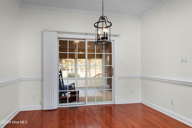 empty room featuring crown molding, an inviting chandelier, wood finished floors, and baseboards