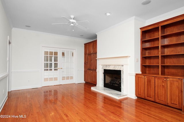 unfurnished living room with crown molding, light hardwood / wood-style flooring, ceiling fan, a fireplace, and french doors