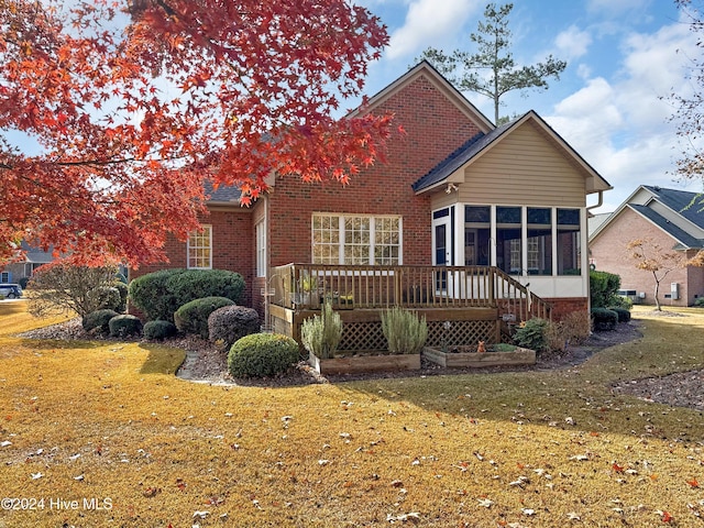 back of property with a wooden deck, a yard, and a sunroom