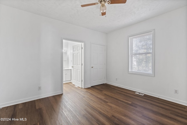 unfurnished bedroom featuring ensuite bath, ceiling fan, dark wood-type flooring, and a textured ceiling