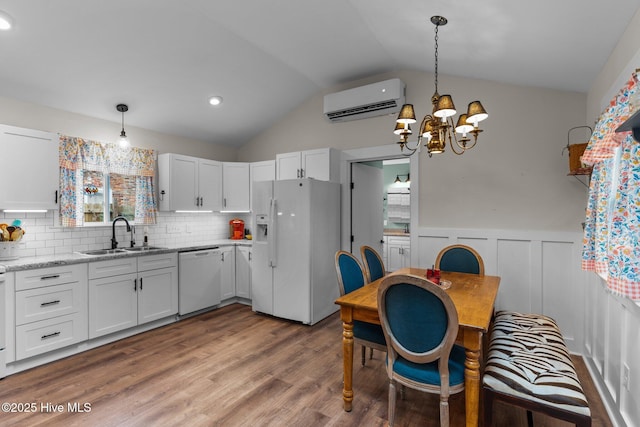 kitchen with sink, white appliances, hanging light fixtures, a wall unit AC, and white cabinets