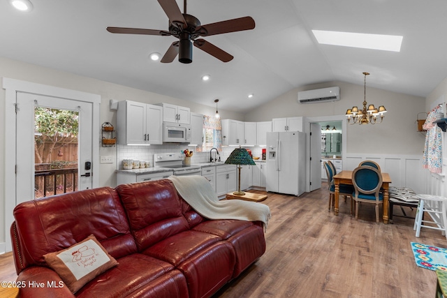 living room with sink, vaulted ceiling with skylight, a wall mounted AC, light hardwood / wood-style floors, and ceiling fan with notable chandelier