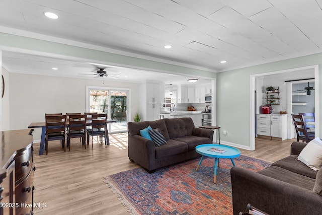 living room featuring crown molding, ceiling fan, sink, and light wood-type flooring