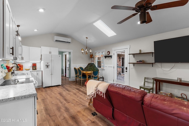 living room with lofted ceiling with skylight, ceiling fan with notable chandelier, sink, a wall unit AC, and light hardwood / wood-style flooring