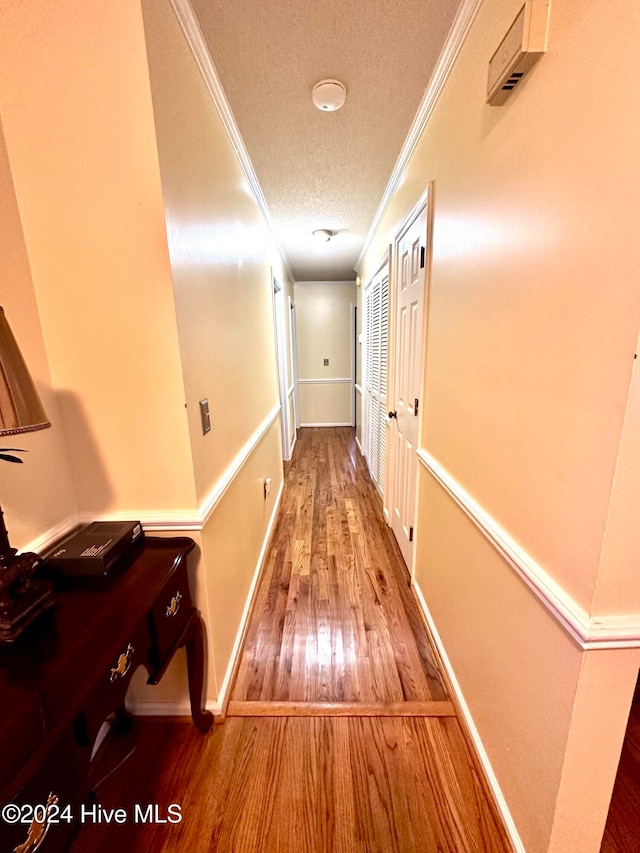 corridor with a textured ceiling, wood-type flooring, and ornamental molding