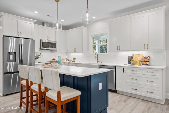 kitchen featuring stainless steel appliances, blue cabinets, light hardwood / wood-style floors, white cabinetry, and hanging light fixtures