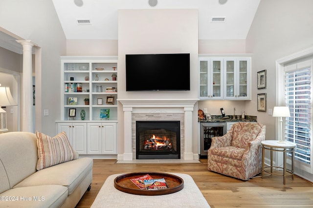 living room with wine cooler, vaulted ceiling, decorative columns, and light wood-type flooring