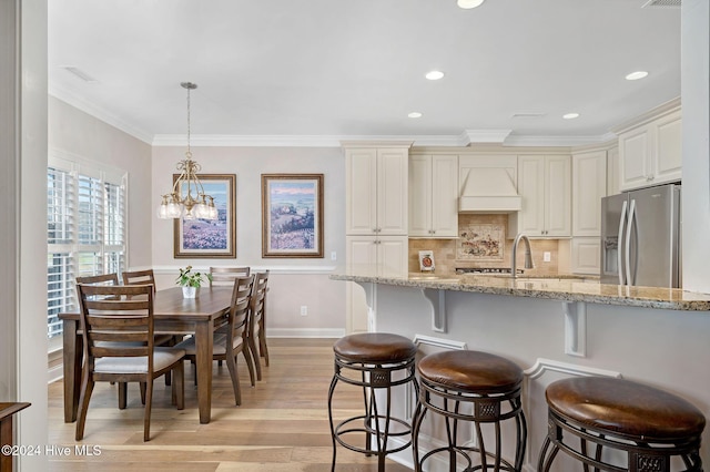 kitchen featuring light stone counters, hanging light fixtures, ornamental molding, stainless steel fridge, and light hardwood / wood-style floors