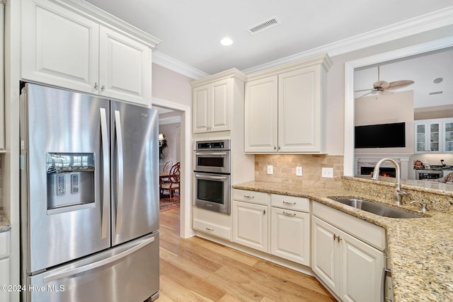 kitchen with sink, backsplash, stainless steel appliances, ornamental molding, and light stone countertops