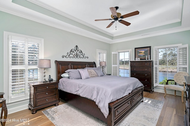 bedroom with ceiling fan, ornamental molding, a tray ceiling, and light wood-type flooring