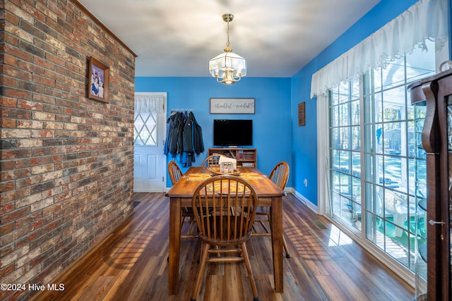 dining space with dark hardwood / wood-style flooring, a chandelier, and brick wall