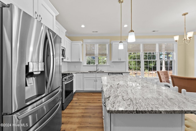 kitchen with a center island, white cabinets, sink, appliances with stainless steel finishes, and decorative light fixtures