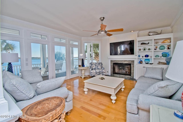 living room featuring light hardwood / wood-style flooring, ceiling fan, crown molding, and a stone fireplace