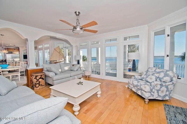 living room featuring ornate columns, ornamental molding, ceiling fan, a water view, and light hardwood / wood-style flooring