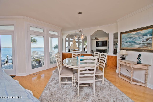 dining room featuring a healthy amount of sunlight, a water view, light hardwood / wood-style floors, and decorative columns