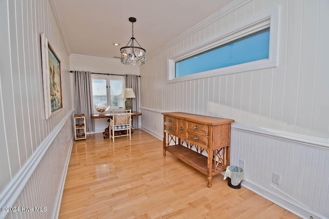 hall with wooden walls, light hardwood / wood-style flooring, ornamental molding, and a notable chandelier