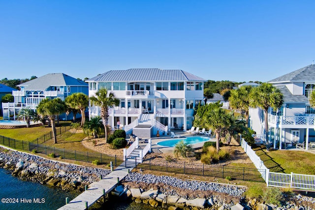 back of property featuring a yard, a fenced in pool, a balcony, and a water view