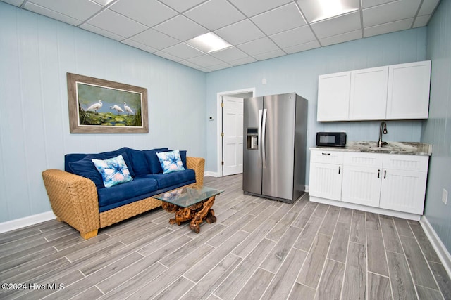 living room featuring a drop ceiling, light wood-type flooring, and sink