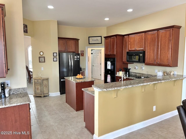 kitchen with a breakfast bar area, recessed lighting, a peninsula, light stone countertops, and black appliances