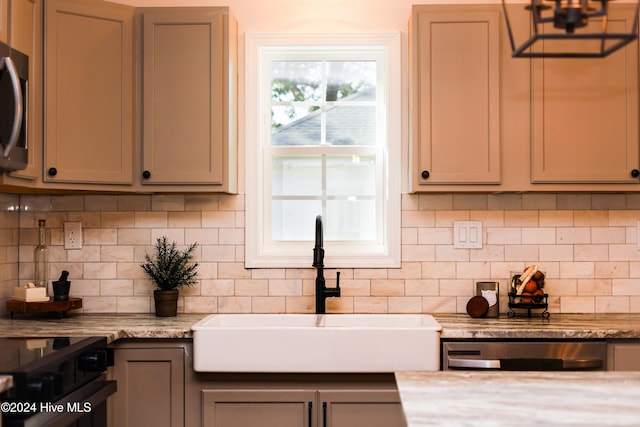 kitchen with gray cabinetry, sink, light stone countertops, appliances with stainless steel finishes, and tasteful backsplash