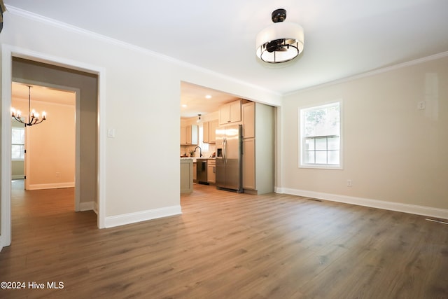 unfurnished living room featuring wood-type flooring, a notable chandelier, crown molding, and sink