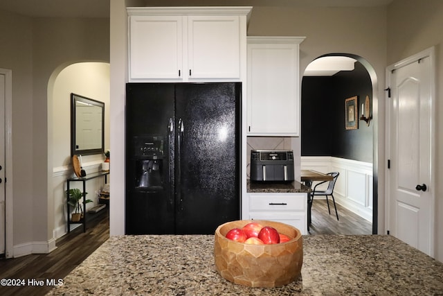 kitchen with white cabinets, black fridge, light stone counters, and dark wood-type flooring