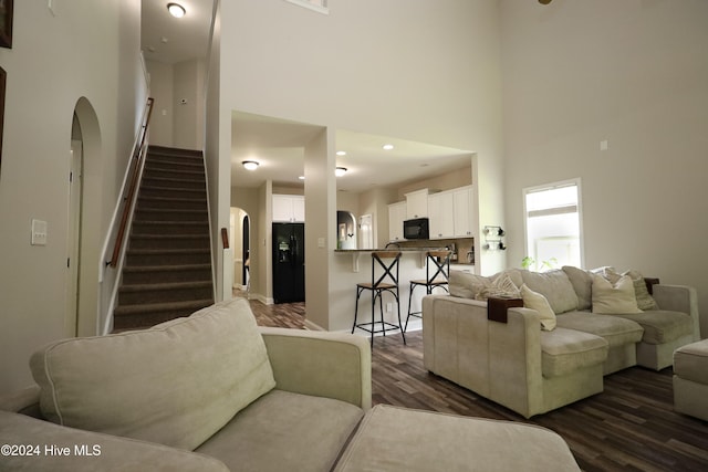 living room with a towering ceiling and dark wood-type flooring