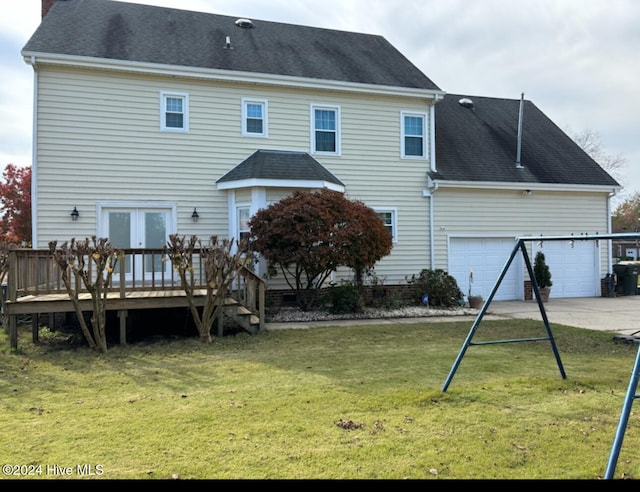 rear view of property featuring a lawn, a garage, and a deck