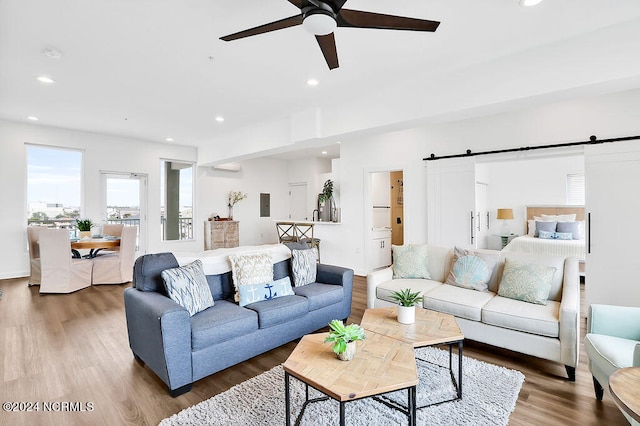 living room with wood-type flooring, a barn door, and ceiling fan