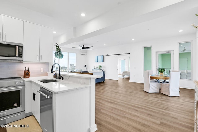 kitchen with kitchen peninsula, appliances with stainless steel finishes, sink, light hardwood / wood-style flooring, and white cabinetry