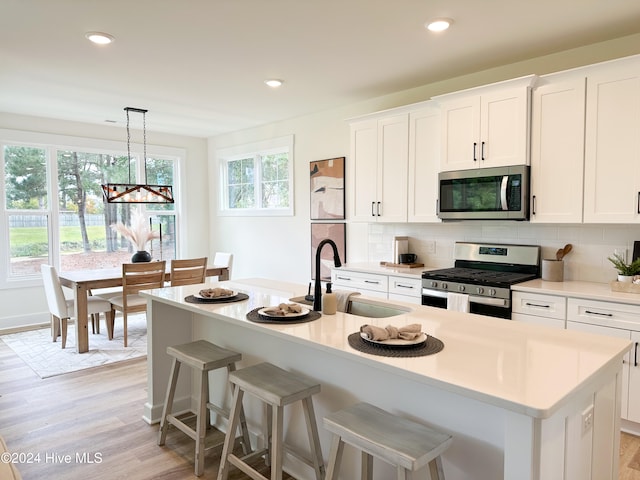 kitchen featuring pendant lighting, sink, stainless steel appliances, an island with sink, and white cabinets