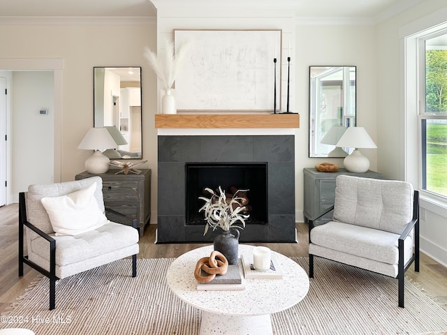 living area with baseboards, wood finished floors, a tile fireplace, and ornamental molding