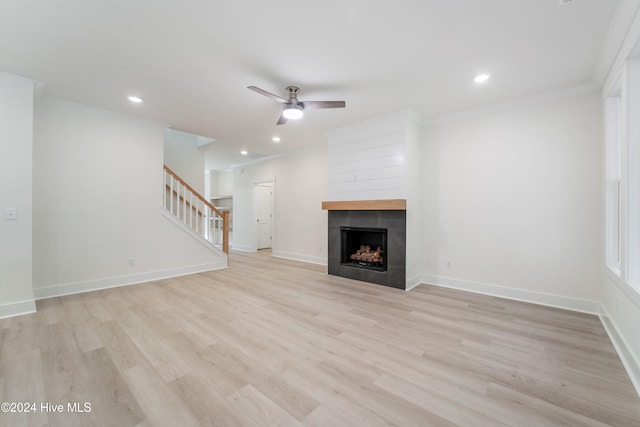 unfurnished living room with a tiled fireplace, ornamental molding, ceiling fan, and light hardwood / wood-style floors