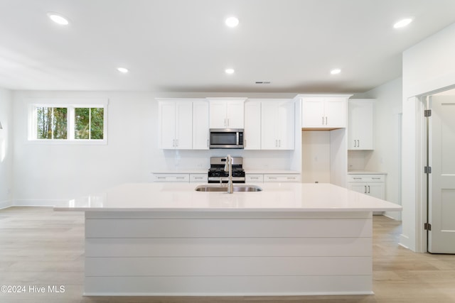 kitchen with white cabinetry, appliances with stainless steel finishes, a kitchen island with sink, and light hardwood / wood-style flooring