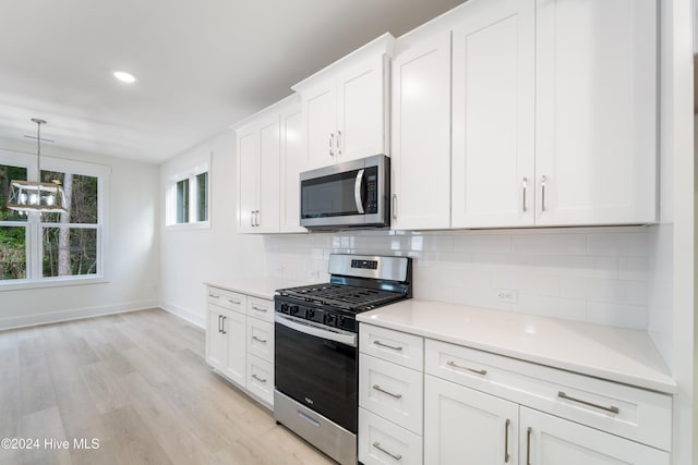 kitchen featuring light wood-type flooring, stainless steel appliances, white cabinets, light countertops, and decorative backsplash