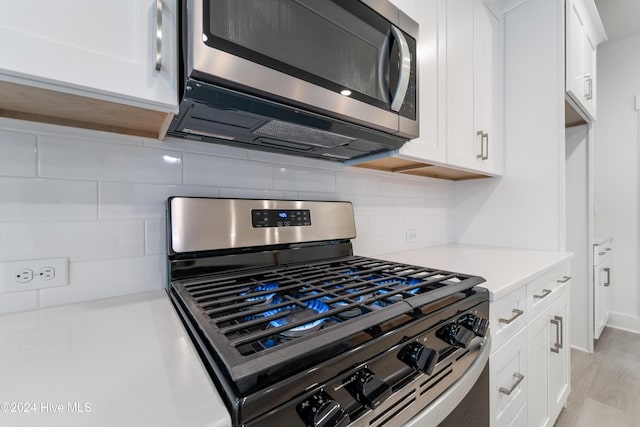 kitchen with light countertops, decorative backsplash, light wood-style flooring, white cabinets, and stainless steel appliances