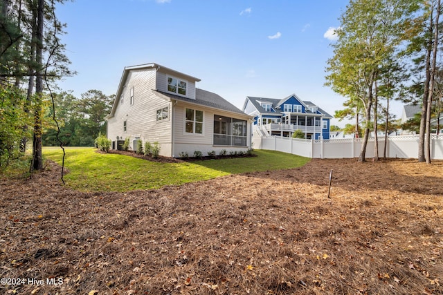 rear view of house with a sunroom, a lawn, central AC unit, and fence