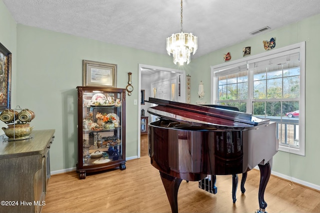 miscellaneous room with an inviting chandelier, a textured ceiling, and light wood-type flooring