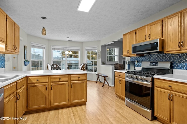 kitchen featuring a wealth of natural light, hanging light fixtures, stainless steel appliances, and light hardwood / wood-style floors