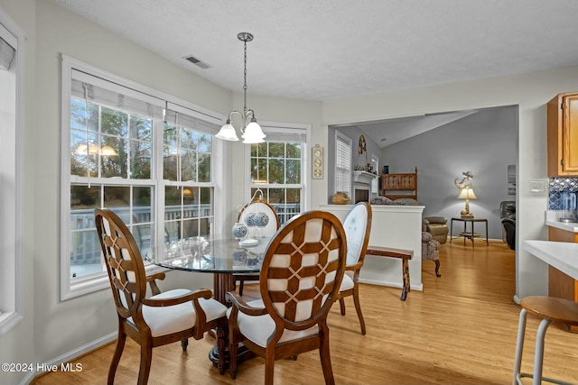 dining space featuring a chandelier, a textured ceiling, light wood-type flooring, and vaulted ceiling