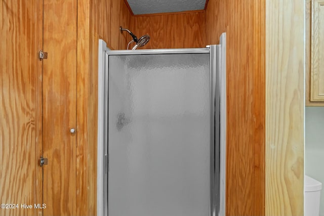 bathroom featuring wood walls, toilet, a shower with shower door, and a textured ceiling