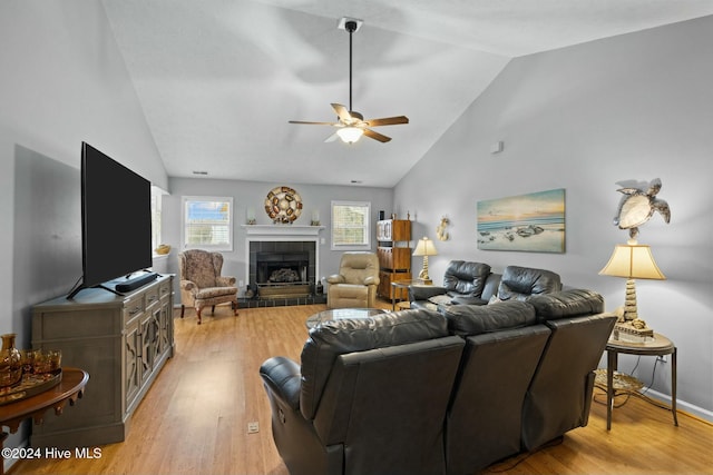 living room with a tile fireplace, light wood-type flooring, high vaulted ceiling, and ceiling fan