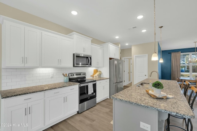 kitchen with appliances with stainless steel finishes, a kitchen breakfast bar, sink, hanging light fixtures, and an island with sink