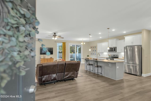 kitchen with white cabinetry, hanging light fixtures, stainless steel appliances, an island with sink, and a breakfast bar