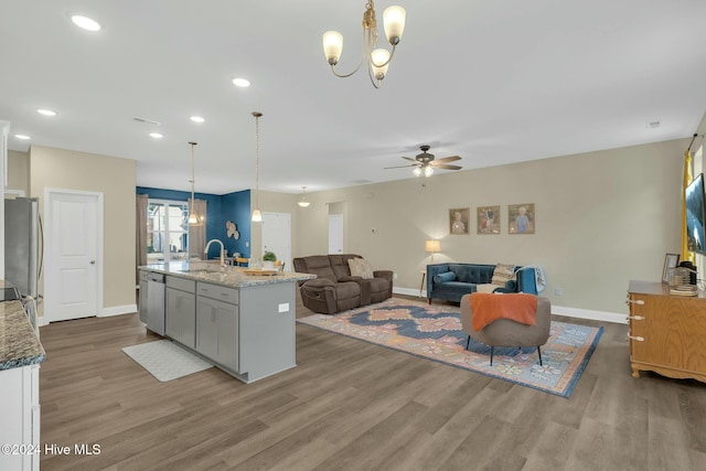 kitchen with light stone countertops, hardwood / wood-style floors, decorative light fixtures, and a center island with sink